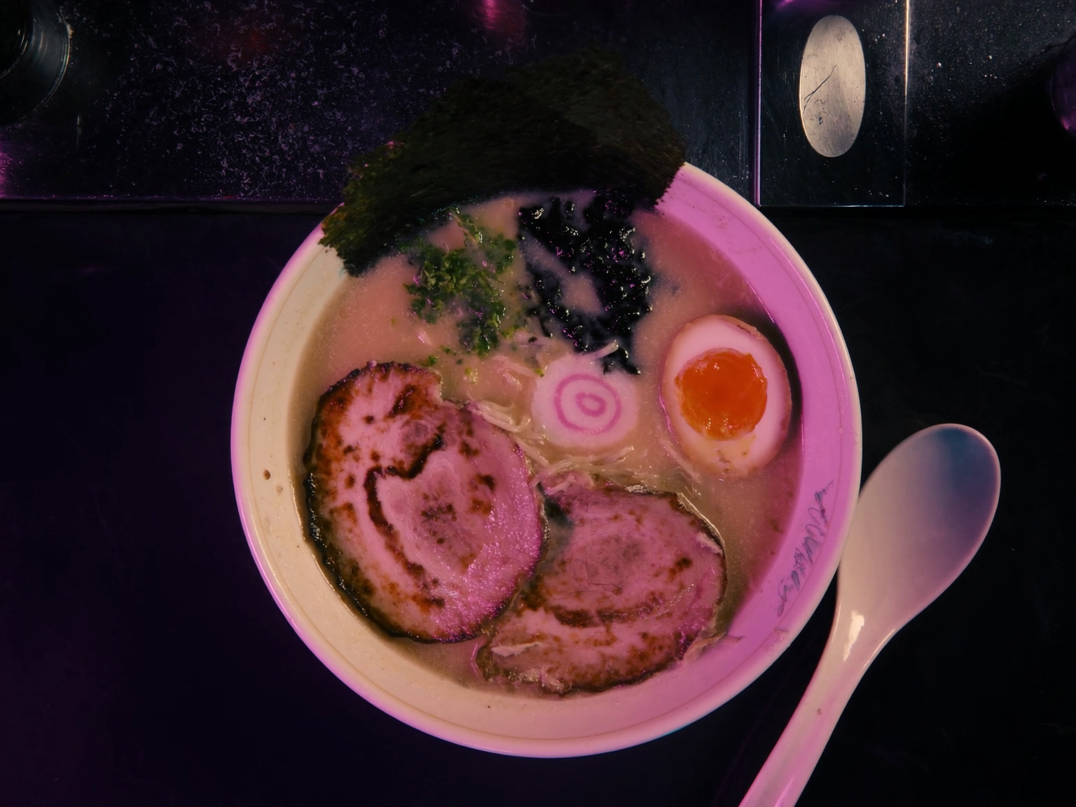 Tonkotsu ramen bowl with chashu and ajitama under neon light