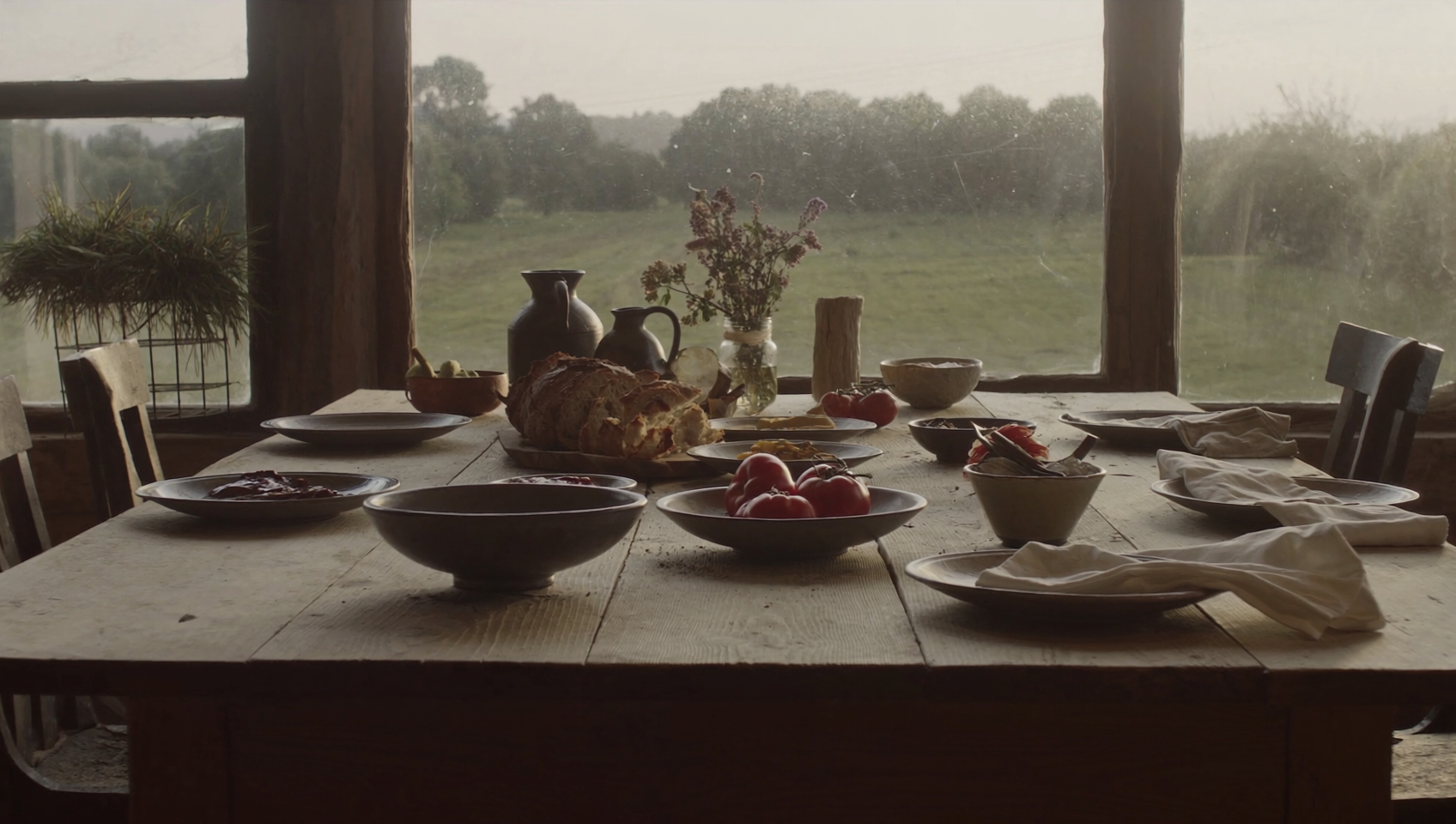 A harvest spread of heirloom tomatoes, bread and ceramics on a weathered farm table in golden light
