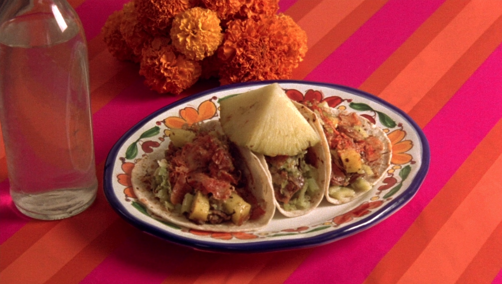 Tacos al pastor with pineapple on a hand-painted talavera plate, on a hot-pink striped tablecloth